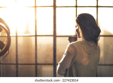 Young Woman Enjoying Cup Of Coffee In Loft Apartment. Rear View