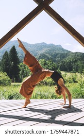 Young woman enjoying freedom on nature. Female doing the yoga pose on wooden pier, outdoors on green landscape background. Travel, Relaxation, Vitality, Outdoor Recreation, Healthy Lifestyle Image.