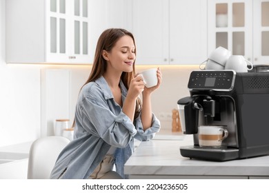 Young woman enjoying fresh aromatic coffee near modern machine in kitchen