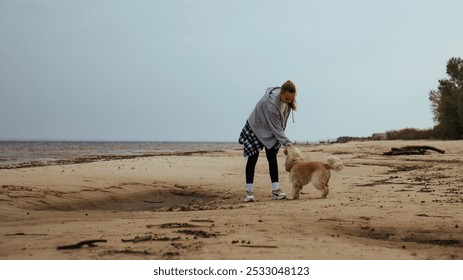 Young woman enjoying a game of fetch with her dog by the sea. The dog runs after a ball, while the girl smiles, reflecting joy and companionship in a beachside environment. - Powered by Shutterstock