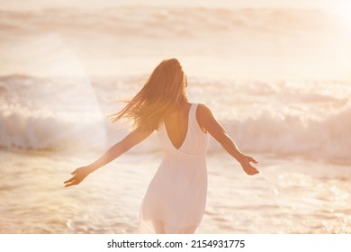 a young woman enjoying her time at the beach. Carefree woman enjoying the sun on the beach. Back of a carefree content woman celebrating and enjoying the sunset on the beach