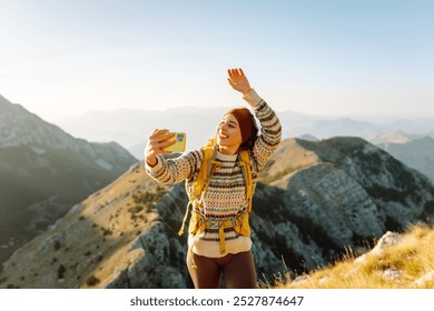 Young woman enjoying a hiking adventure while taking a selfie on a mountain summit during a sunny day. Nature freedom adventure, happy vacation. Blogging. - Powered by Shutterstock