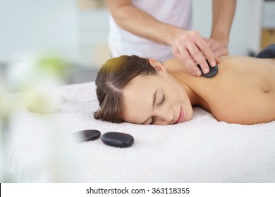 Young woman enjoying a hot rock massage in a spa salon as heated basalt stones are placed on her muscles prior to commencing the massage