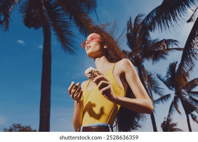 Young woman enjoying ice cream under palm trees on a sunny day with a clear blue sky - Powered by Shutterstock