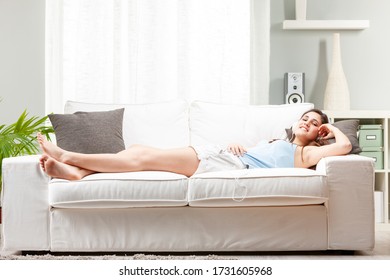 Young Woman Enjoying A Lazy Day At Home Lying On A Comfortable Sofa In A High Key Living Room With Copy Space Smiling At The Camera