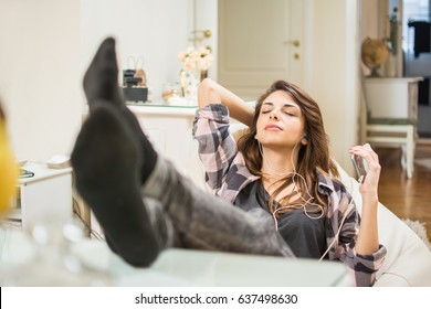 Young woman enjoying listening to music on her mobile device while lying on beanbag at home.