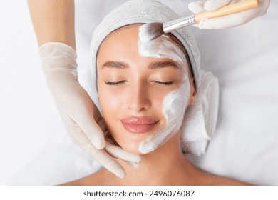 Young woman enjoying luxury professional facial mask treatment, enhancing her skin's radiance. Day at spa, beauty treatment. Top view - Powered by Shutterstock