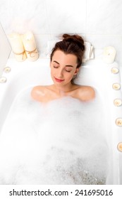 Young Woman Enjoying Lying At The Bath With Foam And Candles