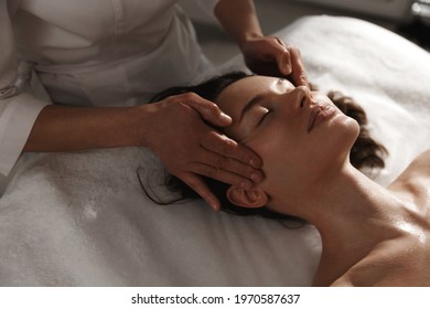 Young woman enjoying massage at spa salon. Beautician rubbing temples of client, smiling girl relaxing during myofascial massaging therapy at beauty clinic, cosmetology procedure - Shutterstock ID 1970587637