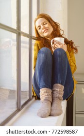 Young Woman Enjoying A Moment Of Peace And Tranquility As She Relaxes On A Window Ledge With A Mug Of Coffee In The Sunshine