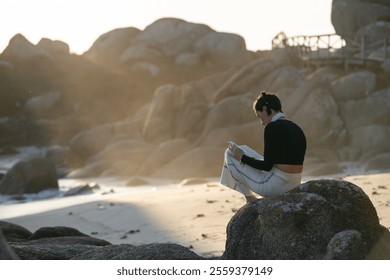 Young woman enjoying a peaceful moment on a rocky beach at sunset, immersed in reading a book while the golden light illuminates the scene - Powered by Shutterstock