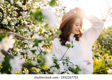 Young Woman Enjoying Scent In Blooming Spring Garden. The Concept Of Youth, Love, Fashion And Lifestyle.