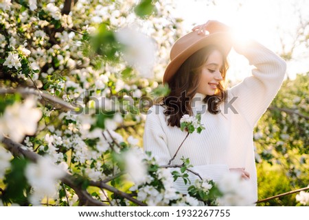 Young woman enjoying scent in blooming spring garden. The concept of youth, love, fashion and lifestyle.