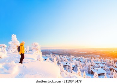 Young woman enjoying stunning view over winter landscape with snow covered trees and wooden huts in Lapland Finland