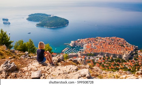 young woman enjoying the view of the Dubrovnik Old Town, sitting on the mountain above the city, Croatia