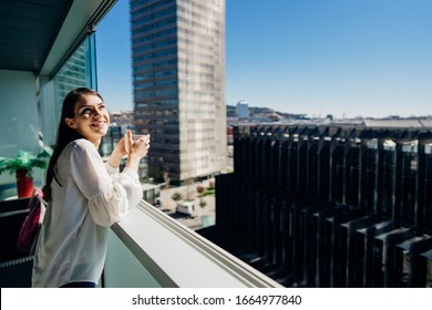 Young Woman Enjoying View On A Sunny Day With Cup Of Coffee/tea On Balcony In Apartment In Industrial/business Area.Positive Young Woman Living In Skyscraper Studio.Ready For The Day.Business Trip