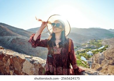 Young woman enjoying the view of a scenic valley in Atacama region, holding her hat on a sunny day