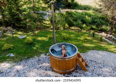 Young Woman Enjoying Wooden Bathtub With A Fireplace To Burn Wood And Heat Water In Backyard In Mountains. High Angle View.