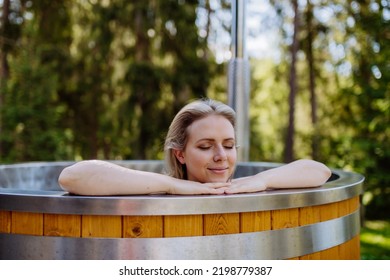 Young Woman Enjoying Wooden Bathtub With A Fireplace To Burn Wood And Heat Water In Backyard In Mountains.