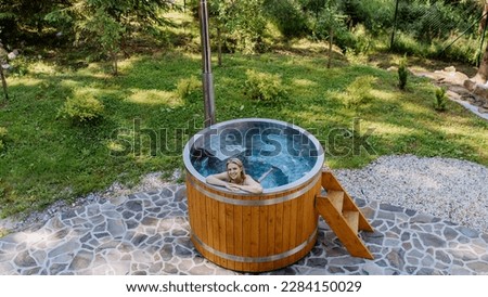 Young woman enjoying wooden bathtub with a fireplace to burn wood and heat water in backyard in mountains. High angle view.