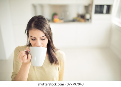 Young Woman Enjoying,holding Cup Of Hot Beverage,coffee Or Tea In Morning Sunlight.Enjoying Her Morning Coffee In The Kitchen.Savoring A Cup Of Coffee Breathing In The Aroma In Bliss And Appreciation