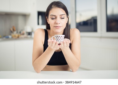 Young Woman Enjoying,holding Cup Of Hot Beverage,coffee Or Tea In Morning Sunrise.Enjoying Her Morning Coffee In The Kitchen.Savoring A Cup Of Coffee Breathing In The Aroma In Bliss And Appreciation