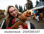 Young woman enjoys holiday market with her playful puppy while holding a stuffed reindeer toy