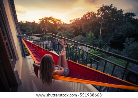 Young woman enjoys sunset relaxing in the hammock on the balcony