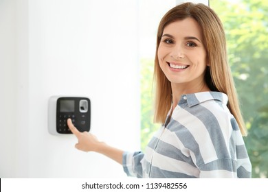 Young Woman Entering Code On Alarm System Keypad Indoors