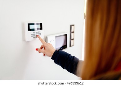 Young Woman Entering Security Code On Home Security Alarm System Keypad