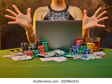 A young woman in an evening dress plays online gambling. There is an open laptop on the table in front of her, cards and chips are laid out. Online casino, strategy games, gambling business.