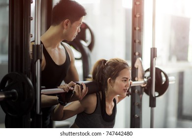 Young Woman Exercise In Gym Stay In Touch Closely To The Trainer Instruction For Proper Action Of Lifting Squat Intakes Weight