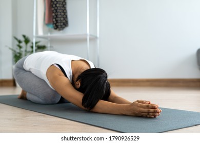 A young woman in exercise wear is doing yoga at home. Woman sitting on the floor leaning forward with her arms stretched. - Shutterstock ID 1790926529