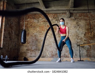 Young Woman Exercising With Battle Ropes At The Gym. Strong Female Athlete Doing Crossfit Workout With Battle Rope During Epidemic COVID-19. Woman Wearing Medical Face Mask In Gym