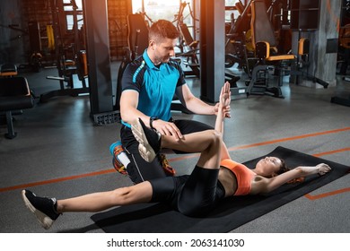 young woman exercising dead bug with personal trainer in gym - Shutterstock ID 2063141030