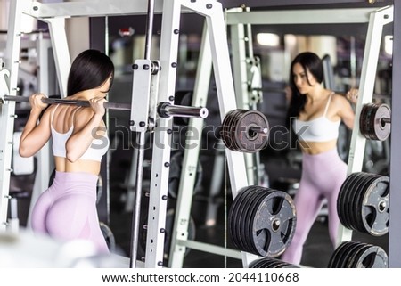 Young woman exercising in gym, doing squats with Olympic barbell