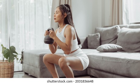 Young woman exercising at home. Asian healthy woman in sportwear doing squat exercise. Home workout concept. - Shutterstock ID 2031836648