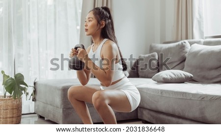 Young woman exercising at home. Asian healthy woman in sportwear doing squat exercise. Home workout concept.