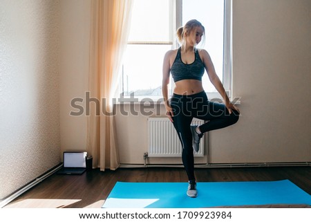 Young woman exercising at home, stretching legs.