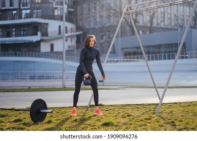 Young Woman Exercising With A Kettlebell Outside At Stadium