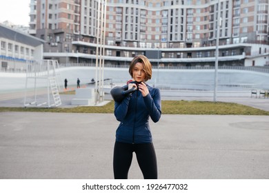 Young Woman Exercising With A Kettlebell Outside At Stadium