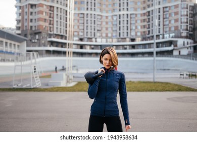 Young Woman Exercising With A Kettlebell Outside At Stadium