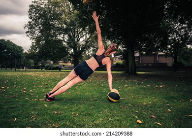 A young woman is exercising with a medicine ball in the park on a cloudy day - Powered by Shutterstock