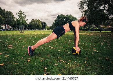 A young woman is exercising with a medicine ball in the park on a cloudy day - Powered by Shutterstock