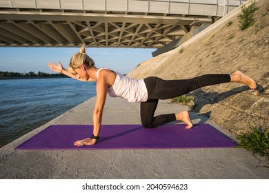 Young Woman Is Exercising Outdoor. She Is Practicing Pilates. Plank With Leg Lift Exercise.