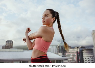 Young woman exercising outdoors on rooftop. Sportswoman stretching her arm outdoors.