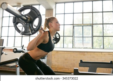 Young Woman Exercising Using Barbell With Heavy Weights In A Health Club.  Female In Sportswear Doing Squats In Gym.