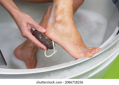 Young woman exfoliating her dry skin heel with a natural pumice stone.