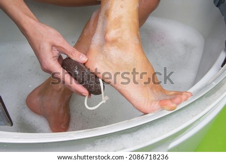Young woman exfoliating her dry skin heel with a natural pumice stone.