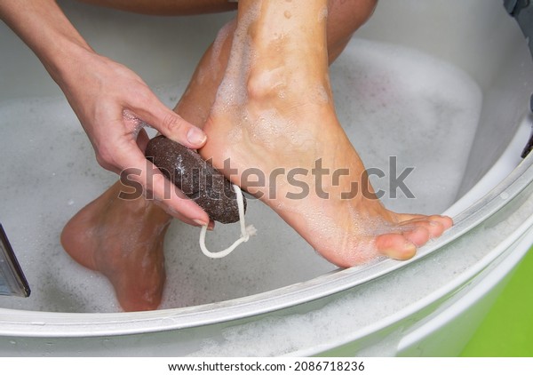 Young woman exfoliating her dry skin heel with a\
natural pumice stone.